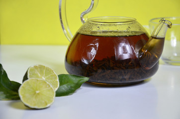 Transparent teapot with black tea, dry tea brewing on the table, bergamot slices, or lemon or lime on a white background