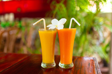 Two glass glasses with freshly squeezed juice and frangipani flower