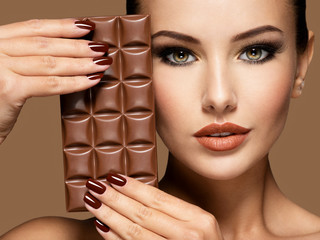 Beautiful woman with brown nails holds bar of chocolate