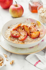 Oat porridge with caramelized apples and nuts on white marble background.