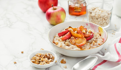 Oat porridge with caramelized apples and nuts on white marble background.