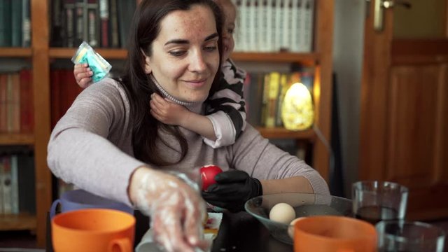 Caucasian mother and little daughter paint Easter eggs in an authentic way with wax candles and paint.