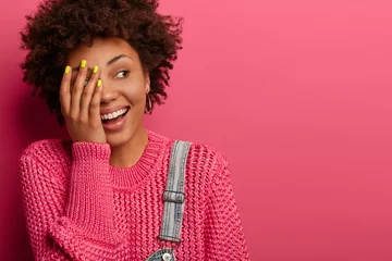 Happy carefree ethnic woman makes face palm, looks happily, hears something hilarious, wears warm jumper, expresses positive emotions, isolated on bright pink background, copy place for promotion © Wayhome Studio