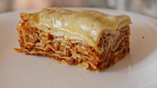 Italian food. Close-up shot of meat lasagna on a white plate. Slow motion.