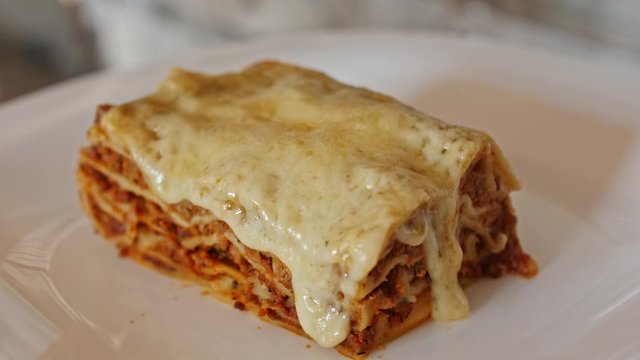 Italian food. Close-up shot of meat lasagna on a white plate. Slow motion.