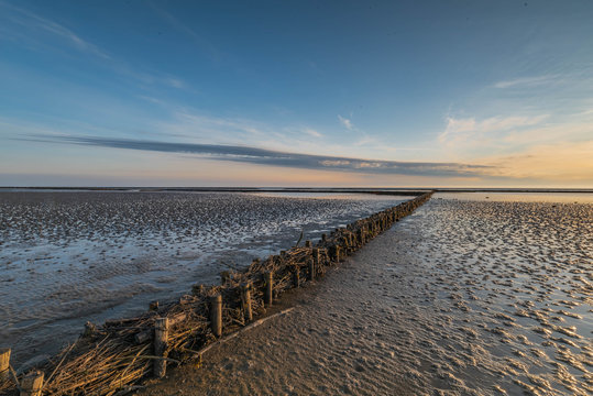An impressive view from the dike foreland near the B&uuml;sum, Westerdeichstrich, Nordfriesland, Schleswig-Holstein Germany, wooden groyne on the beach of North Sea, sunset over the the Wadden Sea, mudflat