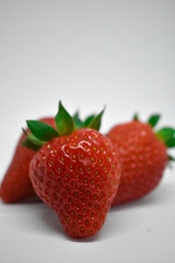 Red strawberries with green leaves, photographed from close up on a white background