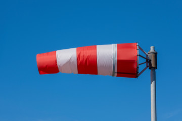 Windsock indicator of wind on runway airport. Wind cone indicating wind direction and force. Horizontally flying windsock (wind vane) with blue sky in the background