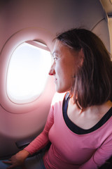 A woman is sitting on a plane and looking out the window.