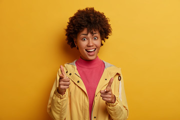 Obraz na płótnie Canvas Hey you, attention. Clients choice concept. Positive African American girl points at camera with happy expression, chooses something, picks someone, wears casual clothes, isolated on yellow background