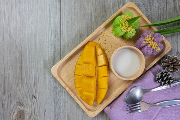 Mango fruit with sweet sticky rice cooked with pandan leave or butterfly pea flower and fried soy and coconut juice in wooden plate on gray wooden. Thai style popular dessert on summer.