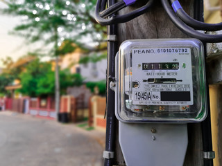 Electricity meter attached to a light pole attached to a plank. Background blurred. Evening light in the village.