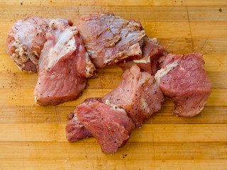 Pieces of pickled raw pork meat on a wooden board.