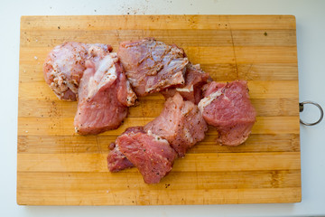 Pieces of pickled raw pork meat on a wooden board.