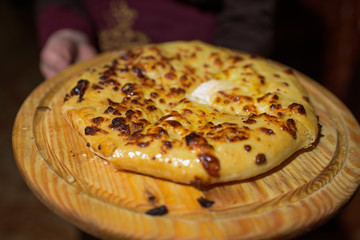 The hand of the waiter who holds a wooden plate with a delicious Ossetian pie.