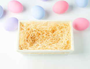 Blank wooden basket with wood wool on white table background with pastel ester eggs