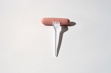Raw sausage with a plastic fork on a white background