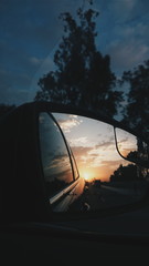 Reflection Of Sunset On Side-view Mirror Against Sky
