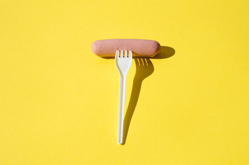 Sausage and white plastic fork on a bright yellow background with hard light