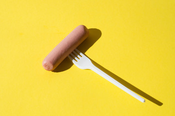 Sausage and white plastic fork on a bright yellow background with hard light