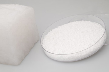 glass laboratory jar with samples of white synthetic rubber and a cube of white rubber next to it on a white background