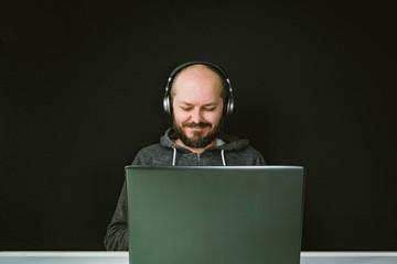 Caucasian man in hoodie and headphones sitting behind the laptop and working, smiling, black...
