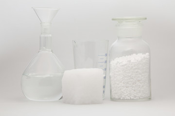 glass laboratory jar with samples of white synthetic rubber and a cube of white rubber next to it on a white background