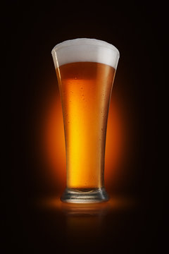 A glass of foamy beer on a glossy tabletop with dark gradient background, spotlight immitation
