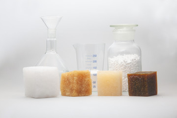 multi-colored samples of a cube of polymer synthetic rubber and laboratory glass jars in the background shot on a white background