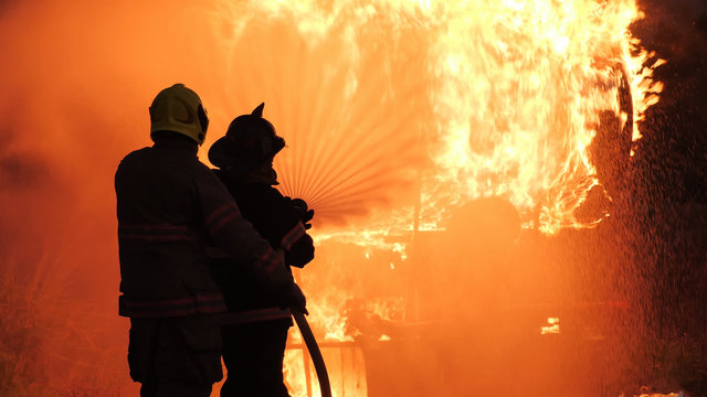 Rear View Of Asian Fireman Wear Fire Protection Suit. Firefighter Spray Water Fighting. Emergency, Fire! At Night..