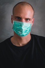 Portrait of young man wearing a medical protection mask from coronavirus with gray background