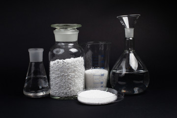 glass laboratory jar with samples of white synthetic rubber and a cube of white rubber next to it on a black background