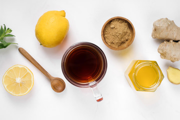 A glass cup of black natural tea with ginger, lemon, mint and honey on wooden white rustic background. Healthy vitamin drink.