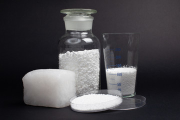 glass laboratory jar with samples of white synthetic rubber and a cube of white rubber next to it on a black background