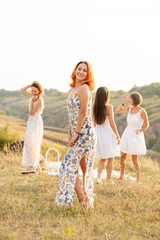 The company of happy female friends having fun and dancing outside in a picnic at hills.