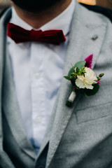 The groom's Burgundy boutonniere . The groom in a jacket.