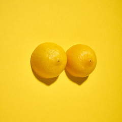 Two yellow lemons on a bright yellow background, imitation of a beautiful female breast. - obrazy, fototapety, plakaty