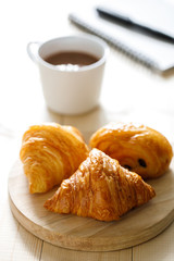 A cup of hot chocolate and croissant on wooden background with notebook.  Work from home.