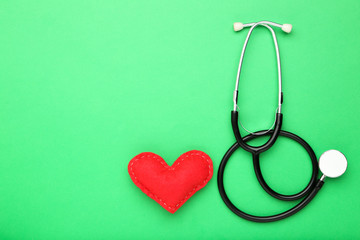 Stethoscope with red fabric heart on green background