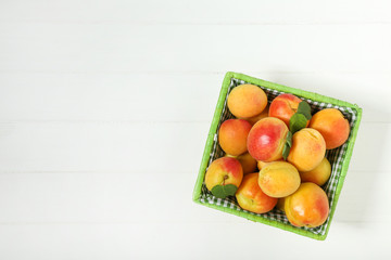 Sweet apricots with green leafs in basket on white wooden table