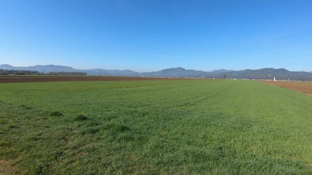 Farming meadow grass field in spring season. In background small town in Slovenia and mountain range. Wide shot, dynamic parallel moving