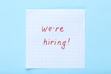 Text We Are Hiring on paper on blue background