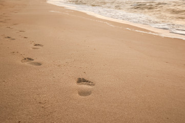 Natural background for text and sand and sea waves. Footprints in the sand from the legs go into the distance. Summer, sea, sunrise.