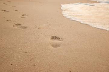 Natural background for text and sand and sea waves. Footprints in the sand from the legs go into the distance. Summer, sea, sunrise.