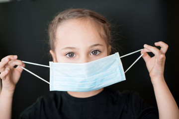 European young girl puts on a medical mask. Conceptual photo on the theme of the covid-2019 pandemic. Isolated on a black background.