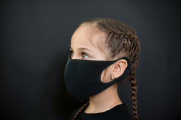 Girl with red eyes and black a medical mask on a black background, copy space. Concept of people who are isolated in a coronavirus quarantine.