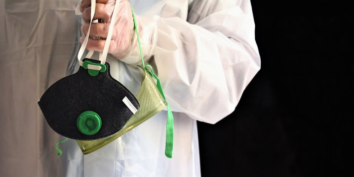 The gloved hand of a worker wearing a waterproof suit holds a mask and splash goggles just removed. Biohazard protection elements