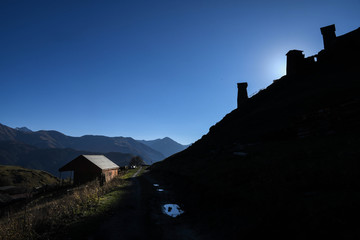 Obraz premium A pathway crosses a house on the left and an ancient tower on the right in Omala - Tusheti