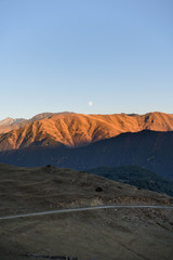 Fototapeta na wymiar The moon rises over a mountain lit by the setting sun in the Tusheti region.