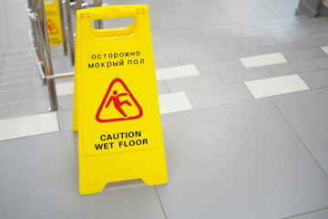 Warning sign with Russian text caution wet floor. A sign near the steps in an office or entertainment center. Cleaning ceramic tiles in a store. Copy space.